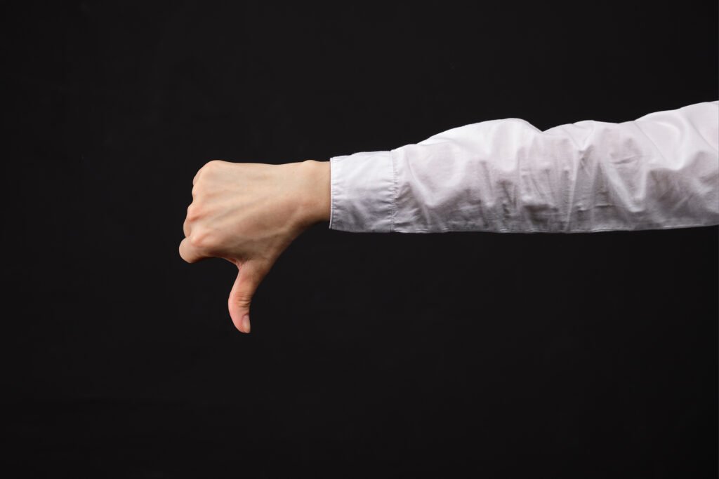Braço de um homem de camisa social manga longa branca fazendo um joinha negativo sobre um fundo escuro, para explicar Mitos sobre a Hiperplasia Prostática Benigna